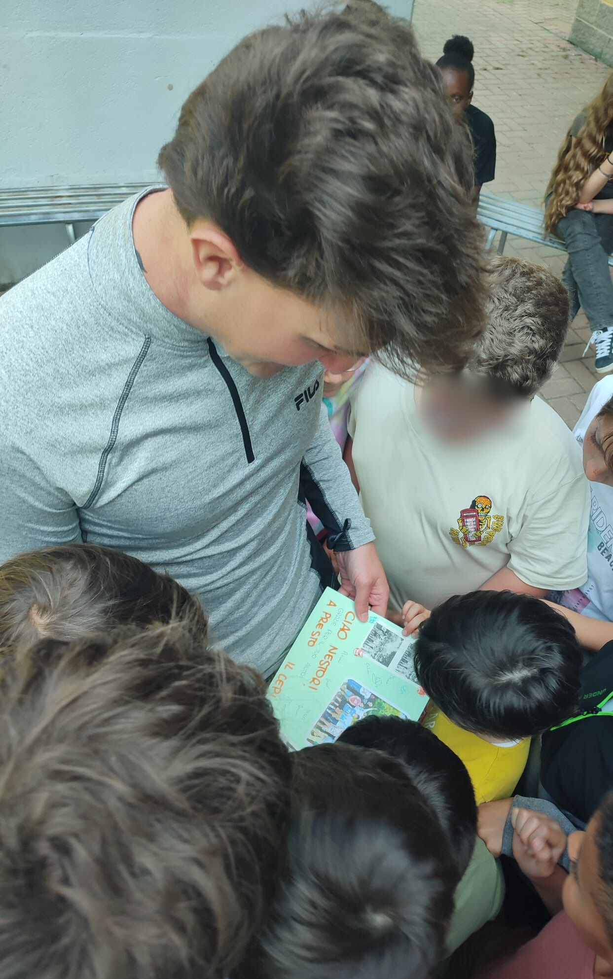 Un grupo de niños y niñas rodea a una persona adulta que les muestra un cartel o cuaderno con dibujos y fotos. Están participando en una actividad educativa o de grupo.