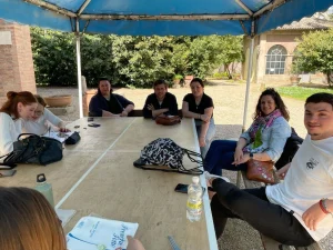 Grupo de profesores y alumnos sonrientes y sentados bajo una carpa