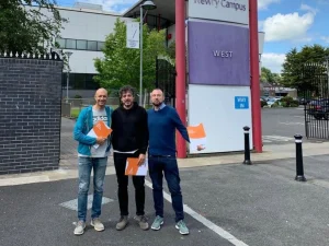 Tres profesores de pie sonrientes delante de universidad en Irlanda